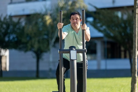 Man with an intellectual disability uses outdoor fitness equipment in a park. His focused