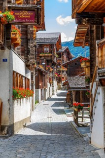 Paved footpath surrounded by old wooden houses, flower boxes on balconies and windows, historic
