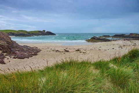 Beach with wavy sea surrounded by rocky headlands and grass, Clachtoll Beach, Clachtoll, Lairg,