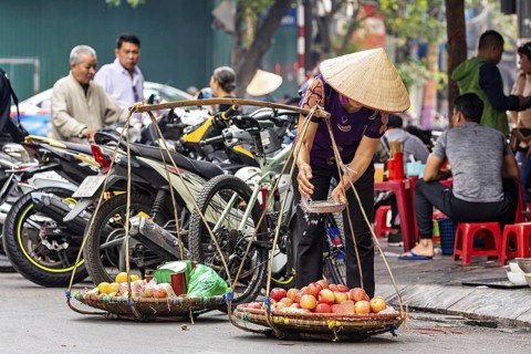 Woman in traditional hat weighing apples at a stall in a busy street neighbourhood, woman selling
