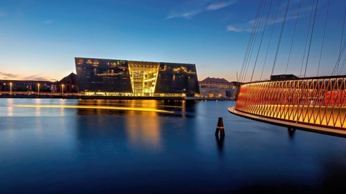 Abendansicht mit beleuchtetem modernen Gebäude und angrenzender Brücke, Kopenhagen, Dänemark,
