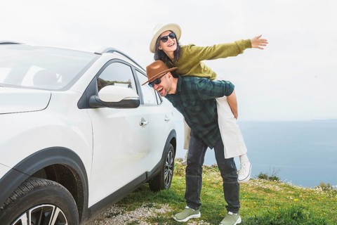 Close up happy couple enjoys holiday time together piggyback check mirror by white SUV during
