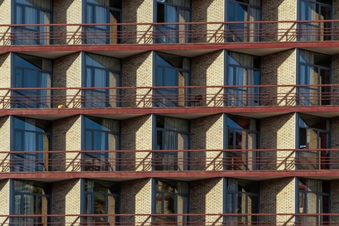 The image captures a modern apartment building with symmetrical balconies, showcased under bright