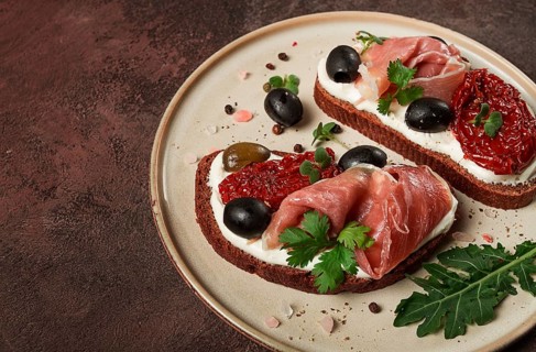 Sandwiches with cheese and prosciutto, dried tomatoes and olives, breakfast on a plate