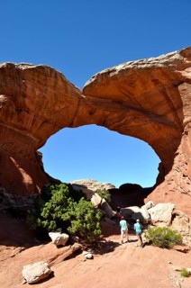 Hikers explore the impressive Broken Arch rock arch on a sunny day, Arches National Park, Utah, USA