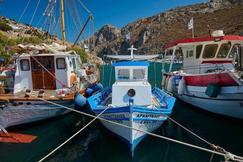 Colourful boats are lying in the harbor against a rocky coastal landscape under a blue sky, Rina,