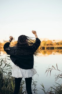 A woman stands by a serene lake during sunset, her arms raised in joy. The golden light reflects