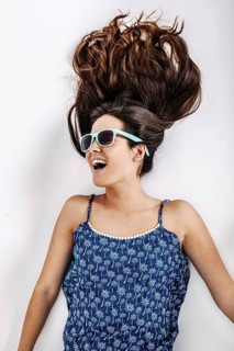 Woman wearing a blue patterned dress and sunglasses, lying on a white background. Her hair is