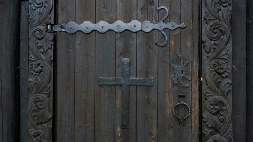 Decorated wooden door with a large metal cross and wrought-iron fittings, backdrop Kristin