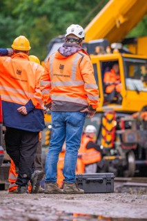 Construction workers in orange protective clothing and white helmets in front of a construction