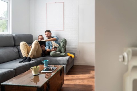 A cheerful gay couple relaxing on a modern gray sofa, engaging with a book. They enjoy quality time