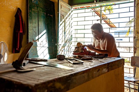 Man carving at a workbench in daylight of an open space using various tools, craftsman leg carving
