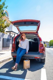 Young woman sitting on the open trunk of a red vehicle in the city street, enjoying a fresh apple