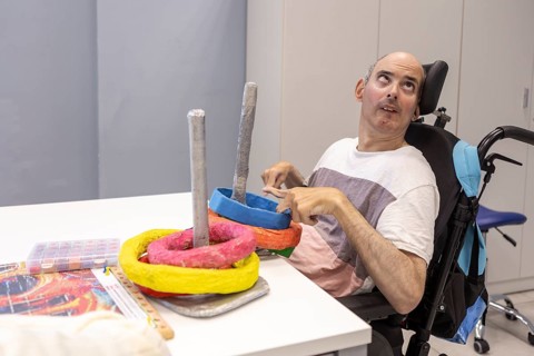A man in a wheelchair participates in activities at a day center, interacting with colorful objects