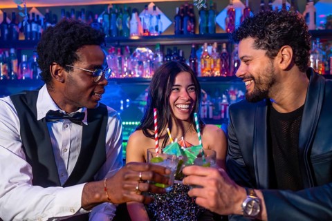 Happy friends enjoying cocktails at nightclub, raising glasses for a celebratory toast in vibrant