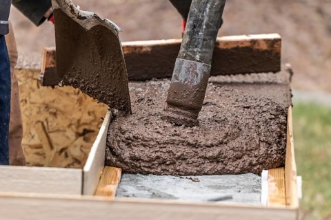 Construction Worker Leveling Wet Cement Into Wood Framing