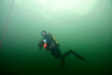 A diver in full gear floats underwater in greenish light, Wreck der Jura dive site, Lake Constance,