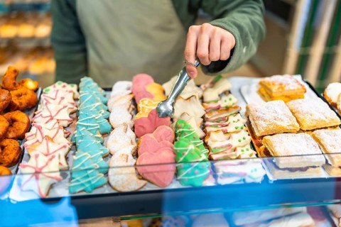 Close-up of a male baker using tongs to place an assortment of colorful Christmas pastries on a