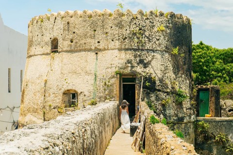 Woman tourist in white dress explores sightseeing the ramparts of the Old Fort in Stone Town,