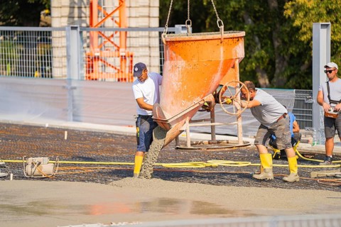Two construction workers empty concrete from a large container on a construction site, Parkhausbau,