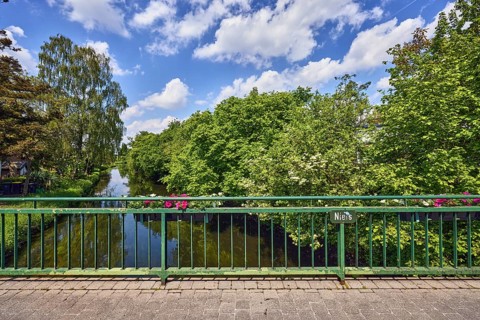 Niers river, car bridge and footbridge, metal railing, riverbank, flower boxes, trees, blue sky,