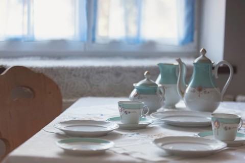 A table set with dishes and cups in front of a window with blue curtains