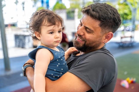 Father holding his young child in an outdoor setting, sharing a tender family moment and expressing