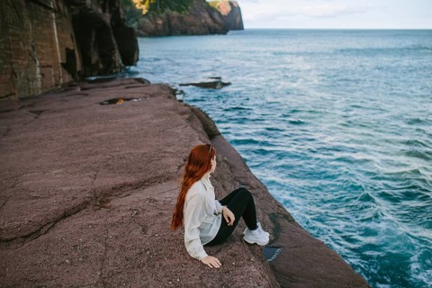 A woman enjoys a serene moment sitting on a rocky ledge overlooking the waves at Flatrock,