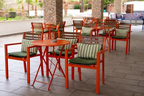 A stylish outdoor seating space features bright orange chairs and tables with striped cushions,