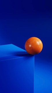 An orange sphere balances elegantly on a vibrant blue geometric shape, creating a striking contrast