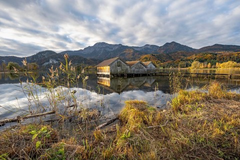 Boathouses in the lake at sunrise, Lake Kochel in autumn with reflection, behind mountain peaks