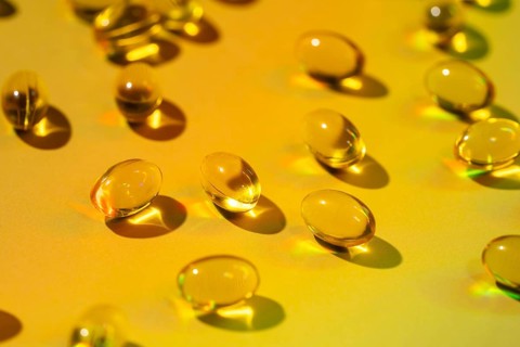 A vivid image showcasing translucent yellow softgel vitamin capsules scattered on a vibrant yellow