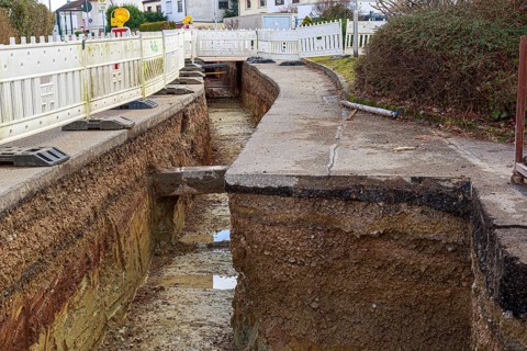 Deep road trench with construction barriers and earthworks in progress