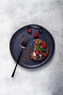 Half-eaten chocolate tartlet, on a plate, stuffed with cottage cheese and berries, breakfast,