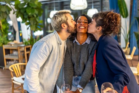 Multi-ethnic friends kissing a latin woman in an outdoor party in a bar terrace