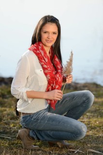 A woman in casual attire kneeling outdoors, holding a plant, and wearing a red scarf and white