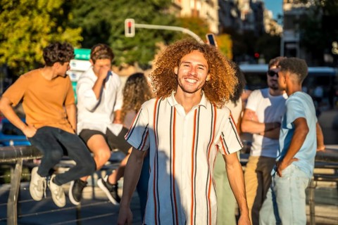 Portrait of smiling young man with curly hair and friends in the city during sunset