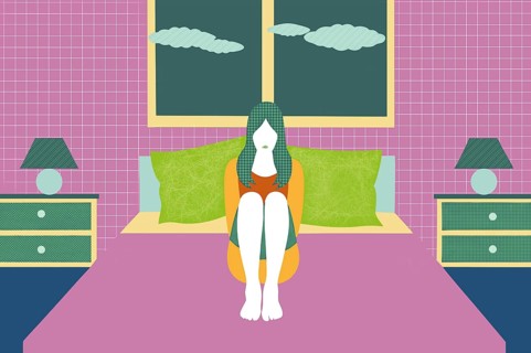 A person is sitting cross-legged on a bed in a vibrant room, surrounded by colorful pillows. This