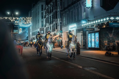 Police on horses patrol illuminated urban street at night, New Year's Eve London, United Kingdom