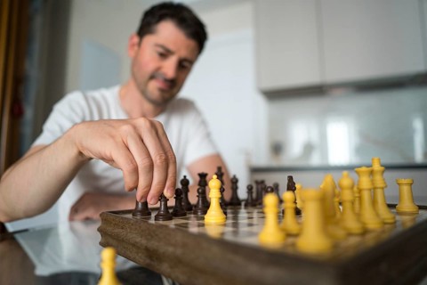 A mature man sits at a table, deeply engaged in a game of chess at home. He thoughtfully considers