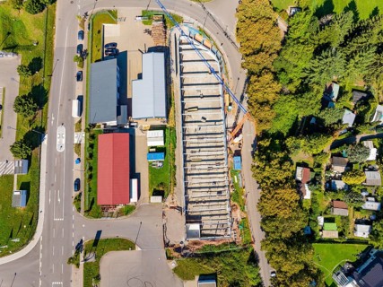 Top view of a construction site surrounded by roads and trees with adjacent residential buildings,