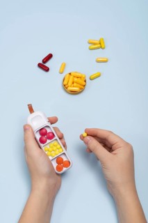 Top view of cropped unrecognizable human hands sorting various colored pills into a white pillbox,