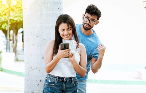 Suspicious man spying on his girlfriend with his cell phone, Jealous boyfriend spying on his