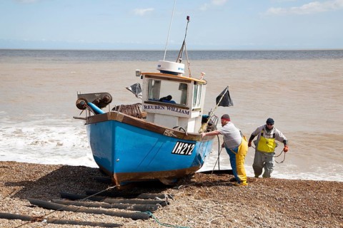Small inshore fishing boat landing on the beach after six hours at sea with a catch of cod and