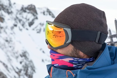 A skier equipped for a ski touring adventure, wearing reflective orange goggles and winter gear in