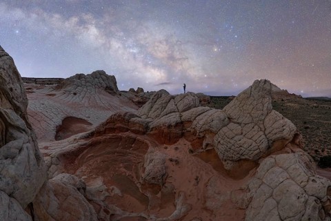 A distant, unrecognizable hiker stands atop a unique rock formation in Utah, USA, under a