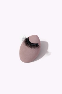 Black false eyelashes is elegantly placed on a makeup sponge against a light background. This setup