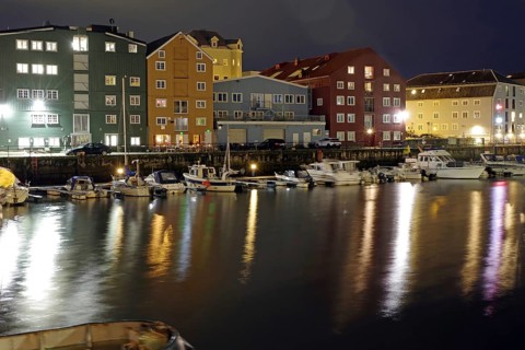 Illuminated colorful buildings are reflected in the water of a nocturnal harbor, Nidelva,