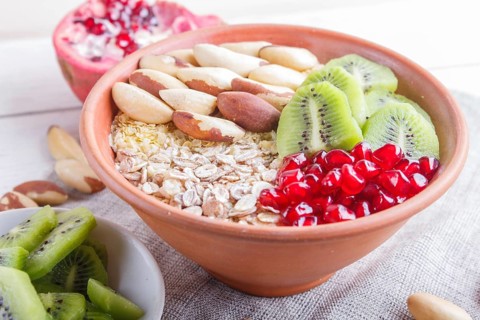 A plate with muesli, kiwi, pomegranate, Brazil nuts on a white wooden background. close up
