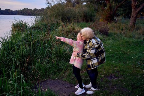 A mother and daughter share a peaceful moment by a river. The girl points toward the horizon,